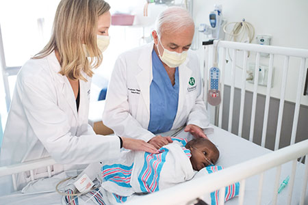 infant in crib with two caregivers standing at the side