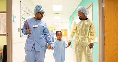 young girl patient walking, holding hand of father and caregiver